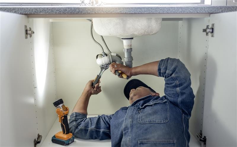 Plumber repairing pipes beneath a bathroom sink in Oakdale